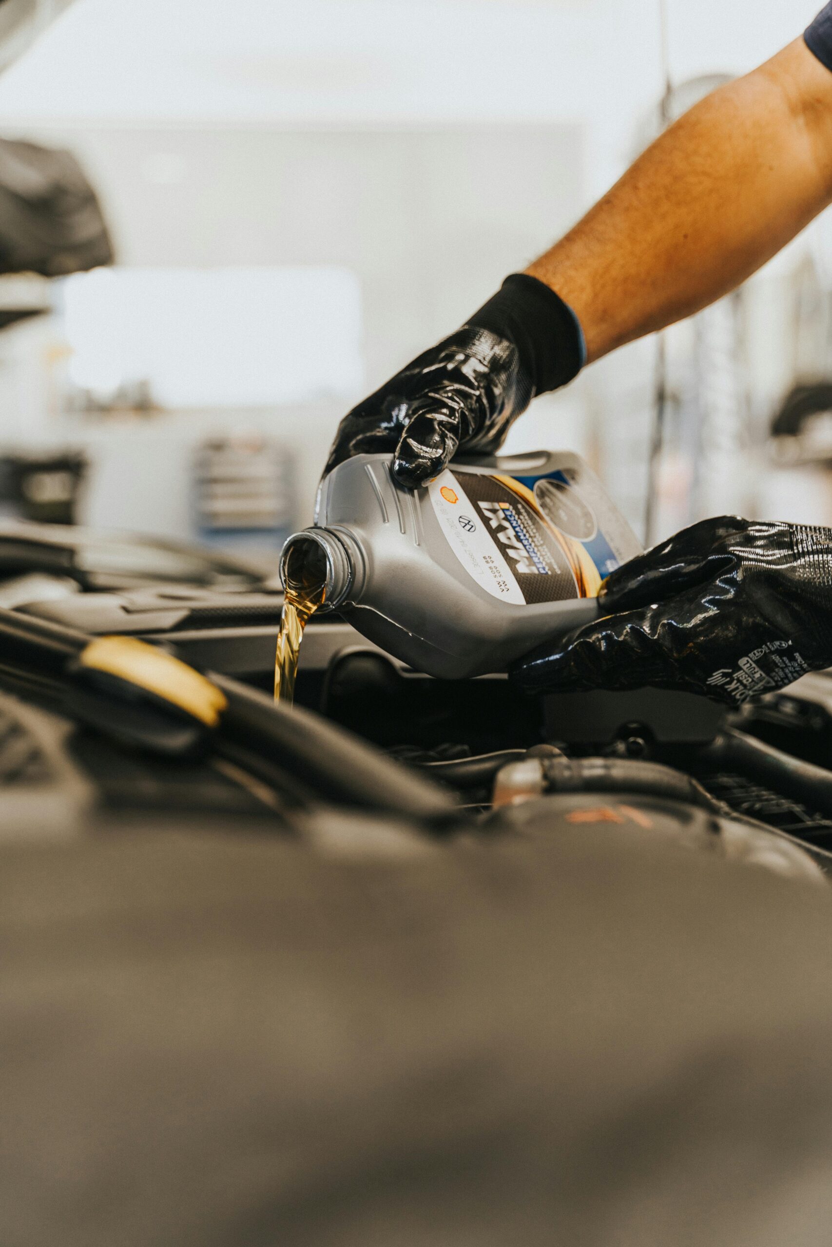 Close-up of a mechanic pouring engine oil into a car engine with gloved hands, indoors.