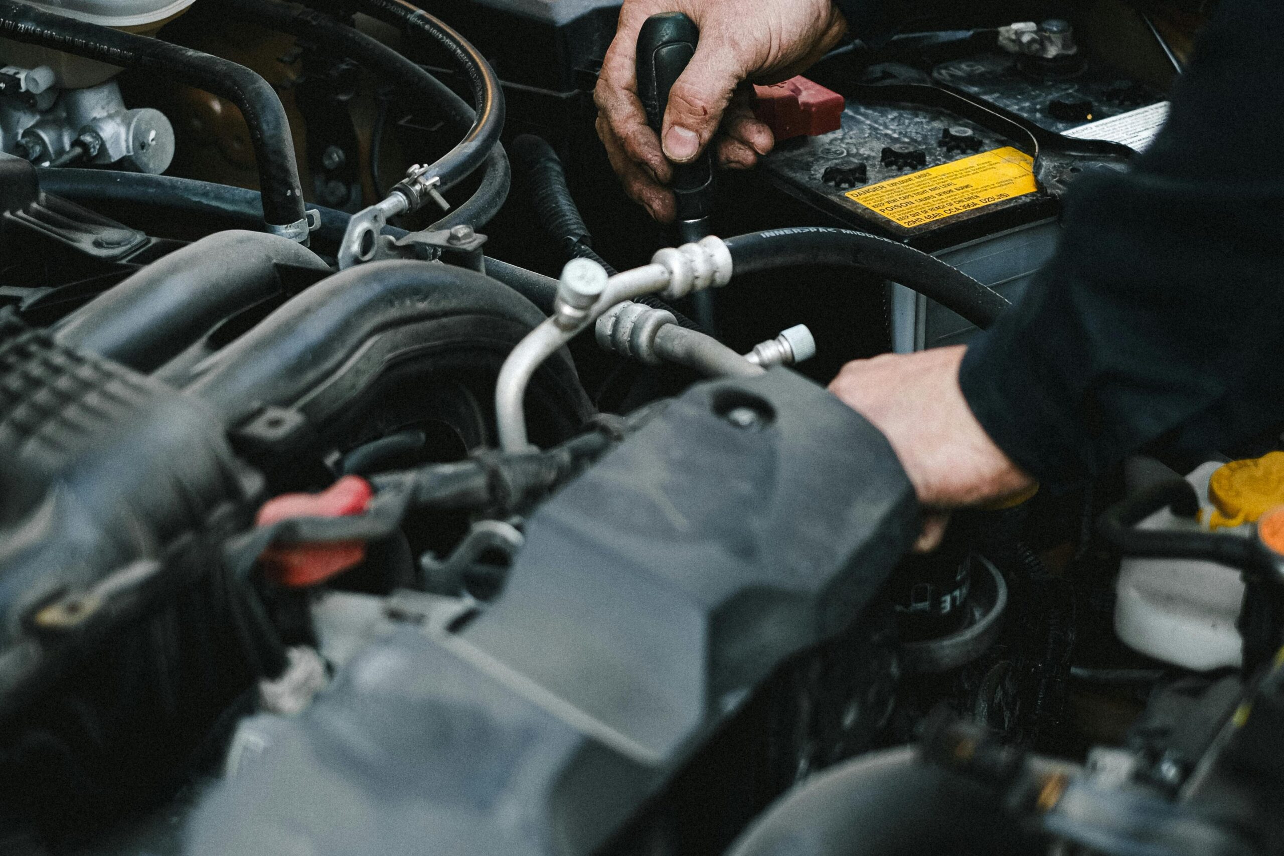 Close-up of a mechanic's hands working on a car engine in an indoor workshop setting.